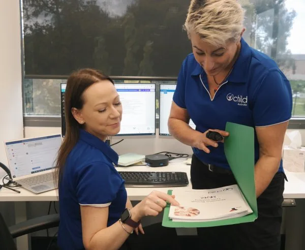 Two woman look at a folder and smile