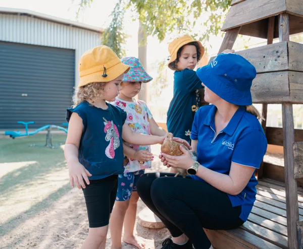 An educator holds a chicken whilst the children pet it