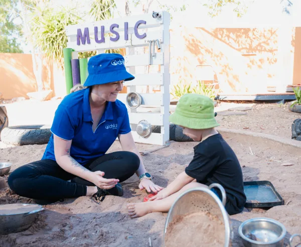 An educator and child play in the sand pit