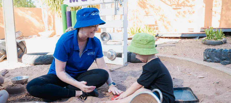 An educator and child play in the sand pit