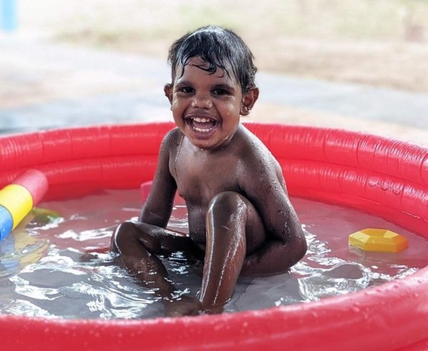 child playing in an outdoor paddling pool while laughing