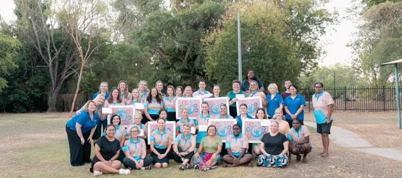 A group of people smile for a photo abnd hold up a photo