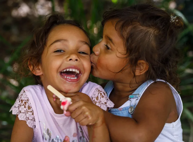two girls outdoors laughing with plants in the background
