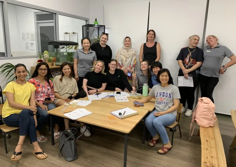 A group of women sitting and standing by a desk smiling for a photo