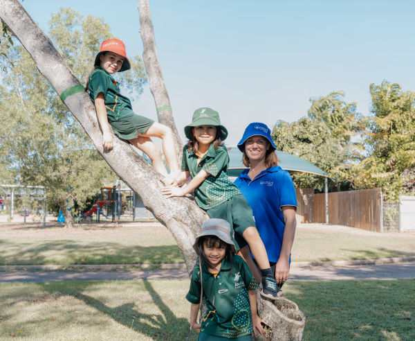 Children and an educator smile whilst climbing a tree