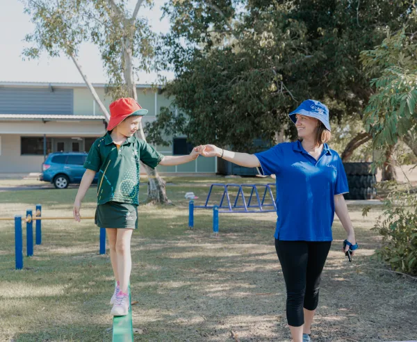 A child walks along a beam whilst holding the educators hand