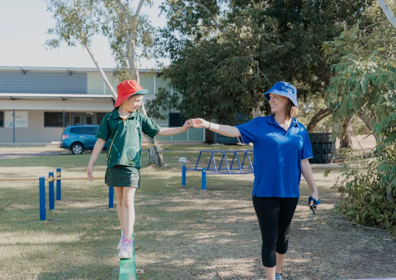 A child walks along a beam whilst holding the educators hand