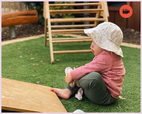 A baby plays outside whilst taking off her shoes