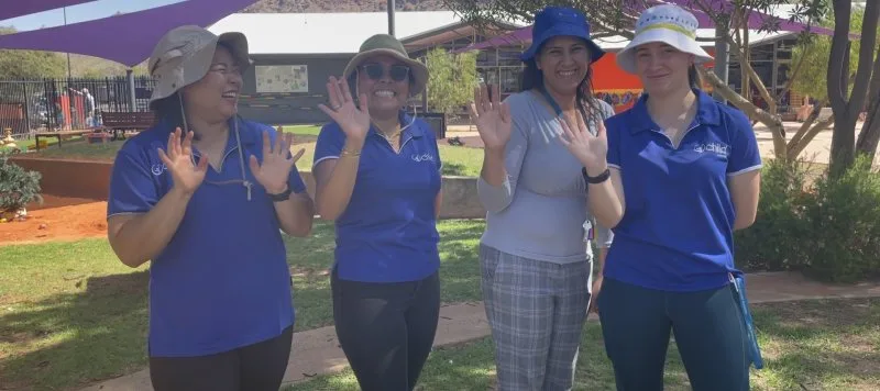 4 employees wave and smile for a photo outside