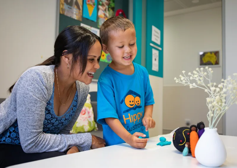 A woman and a child smile together and play with playdoh