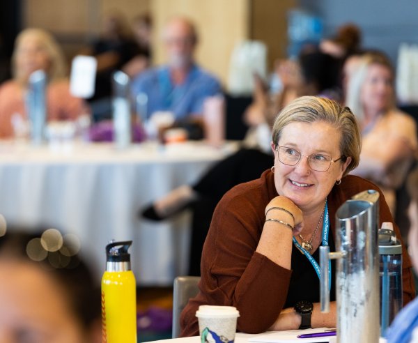 A woman smiles whilst listening to a conference