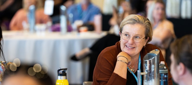 A woman smiles whilst listening to a conference