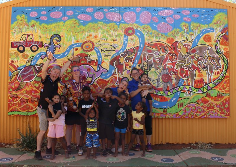 4 staff members and children smile fro a photo in front of artwork