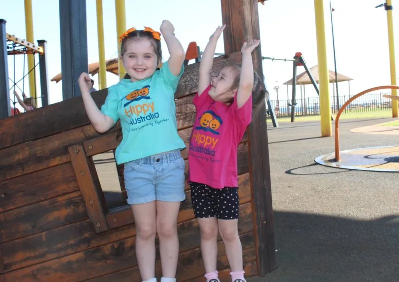 2 kids throw their hands up in the air at the playground