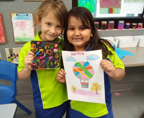 Two children hold up their arts and crafts for a photo and smile