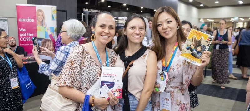 3 woman smile for a photo whilst holding up flyers