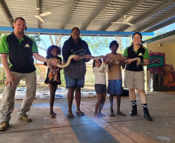 Bagot OSHC learning about reptiles with animal encounters - an image of educators and children holding up a large snake