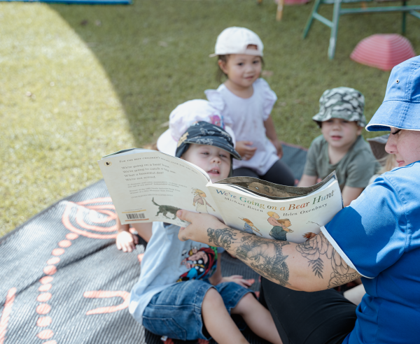 An educator reads a book to children outside