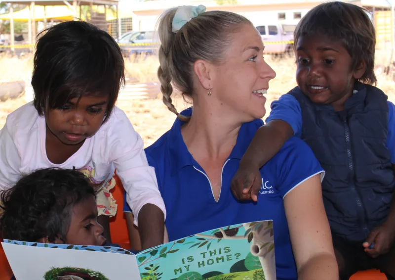 A woman and three kids read a book together