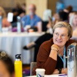 A woman smiles whilst listening to a conference